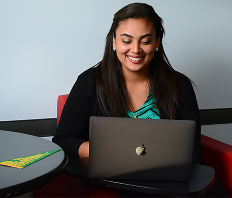 A student sitting in a conference room working on a laptop with a ҹav pennant on the table